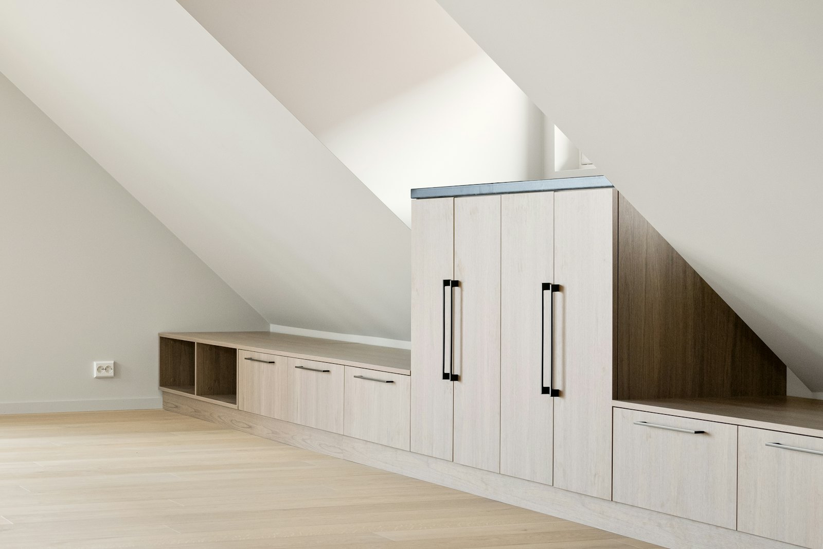 White built-in cupboards and drawers fitted under the sloping ceiling of an attic